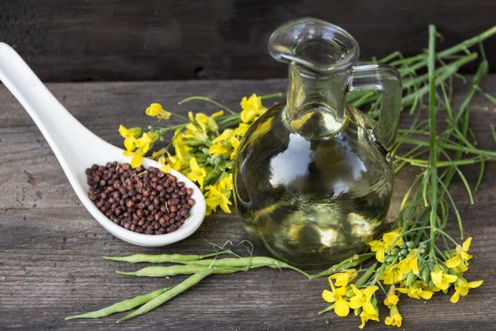 bottle rapeseed oil seeds and flowers on rustic wooden background